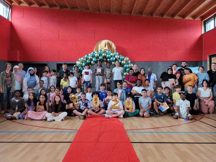 Les élèves de CM2 posent avec l'équipe enseignante devant une arche de ballons installée dans le gymnase.