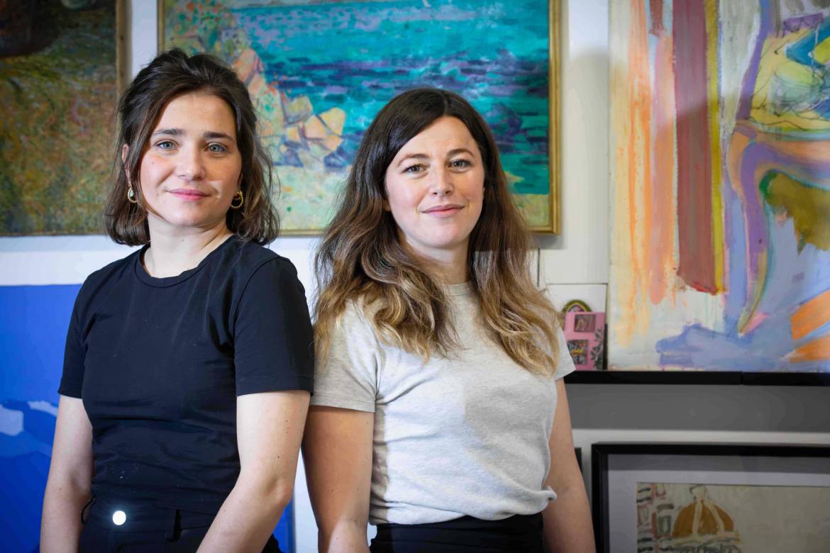 Les deux restauratrices souriantes posent devant les tableaux colorés de leur atelier