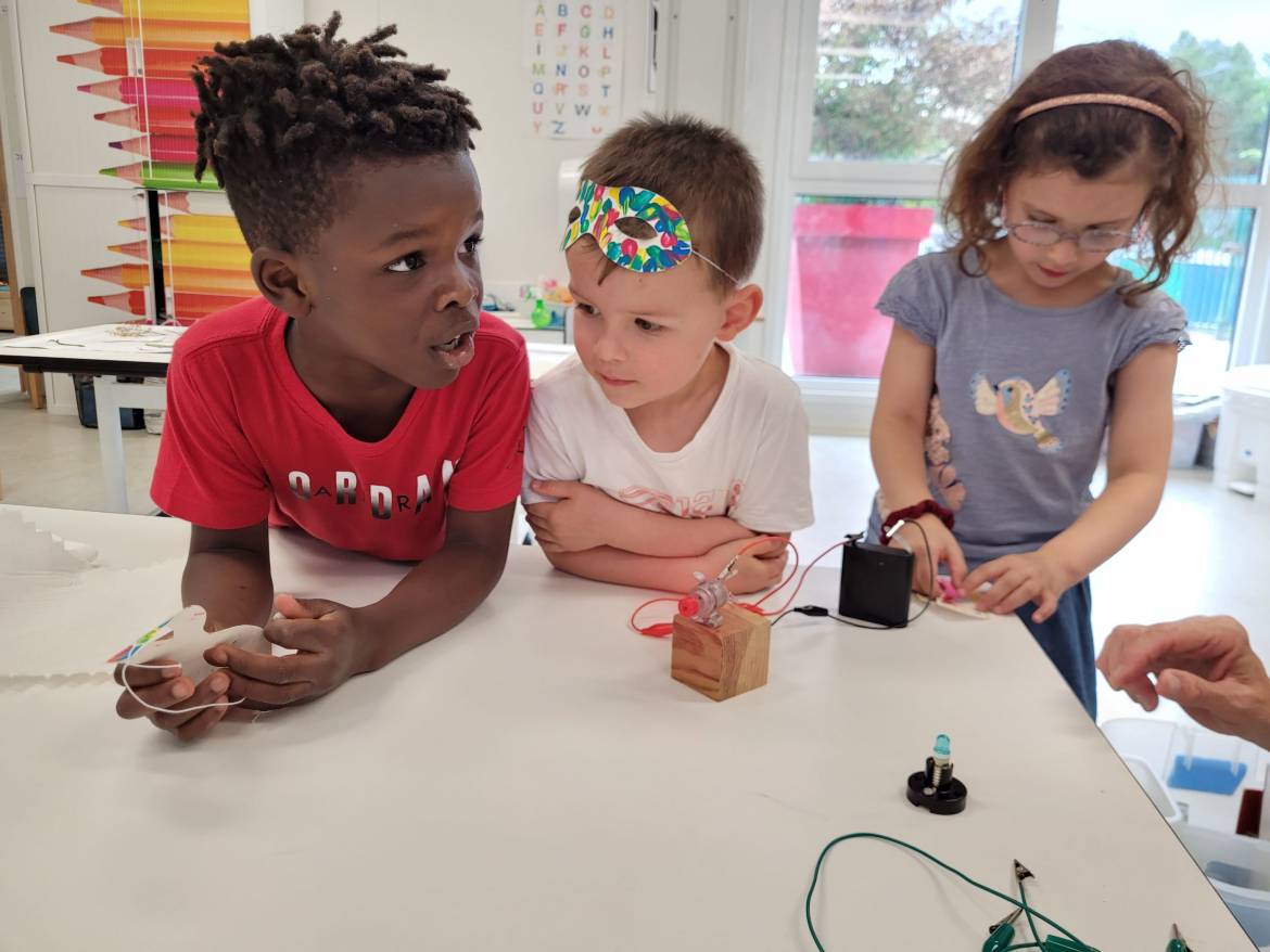 Trois enfants observent le circuit électrique qu'ils ont fabriqué.